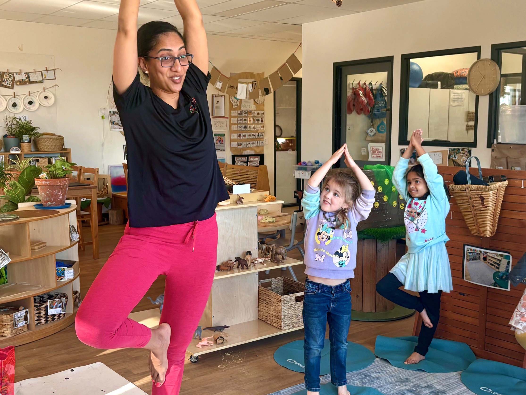 Yoga teacher performing the tree pose with two young children in an early learning centre