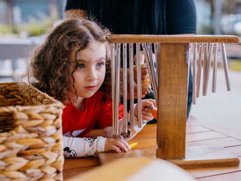 Girl sitting at table looking closing at a chime bar musical instrument 