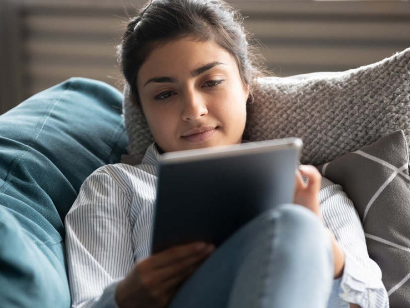 Woman looking relaxing sitting with her legs up on a couch reading on a tablet device