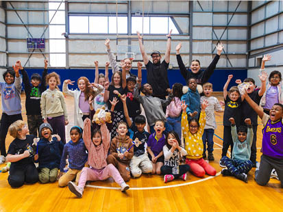 Group photo of OSHC kids and educators in stadium with their hands in the air