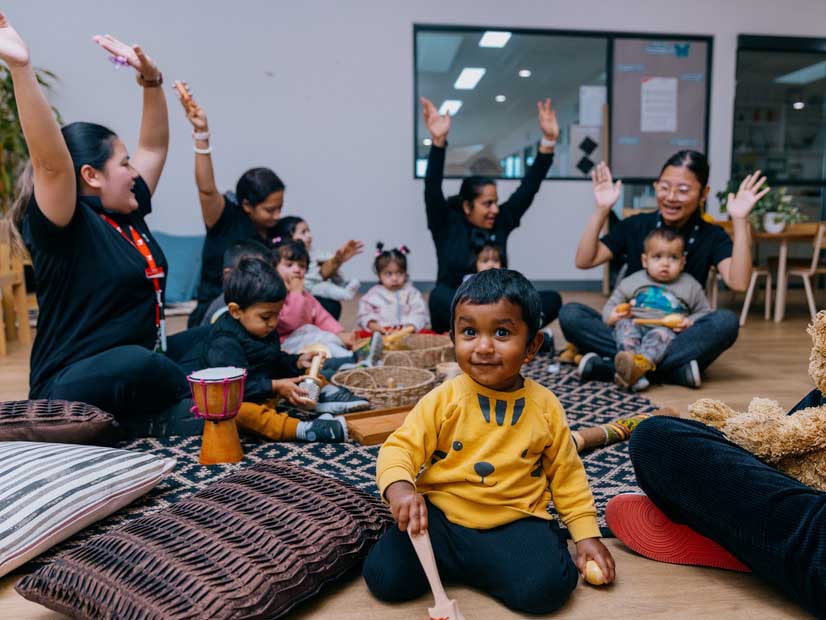 Children sitting in a circle with early learning educators playing musical instruments