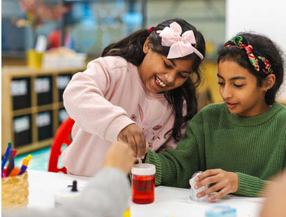 Two school aged girls smiling doing a craft activity together at a table