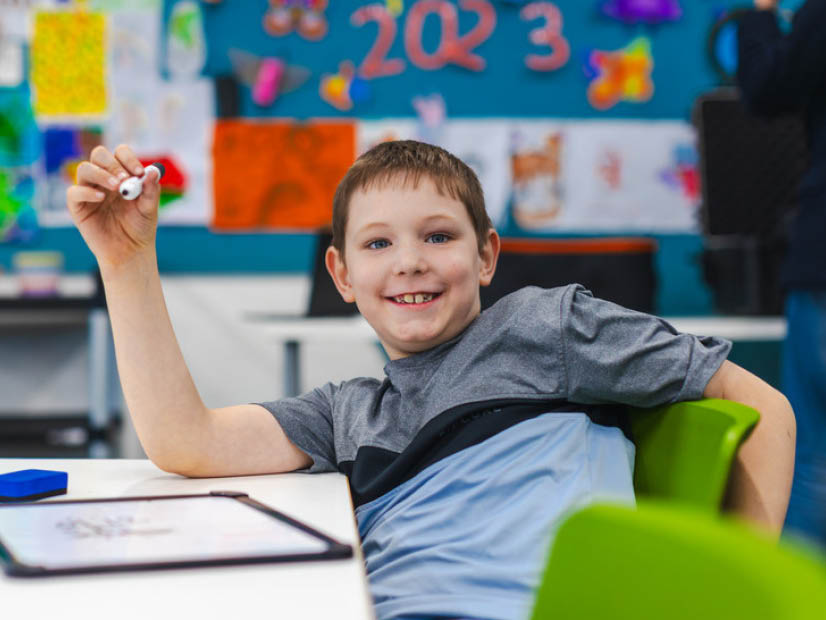 Boy siting at table with his drawing looking up smiling