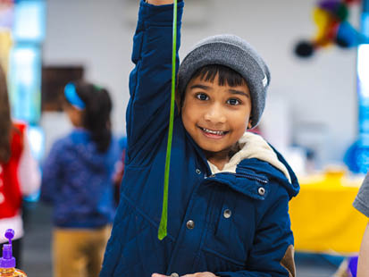 Boy smiling holding up a string of slime in OSCH classroom