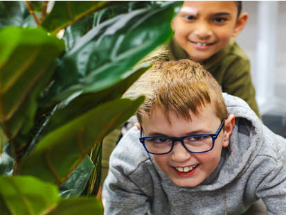 Two boys playing near plants at school holiday program