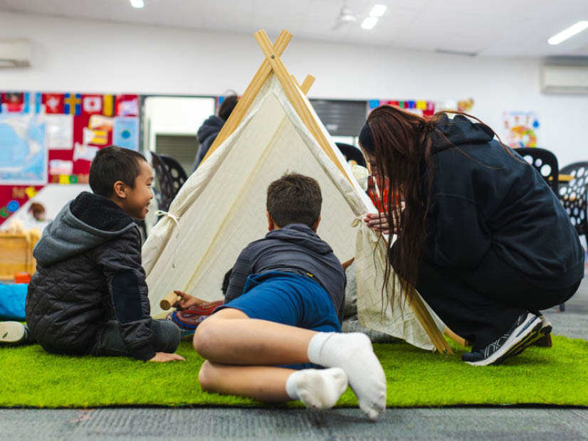 Boys and OSHC educator playing at a teepee tent