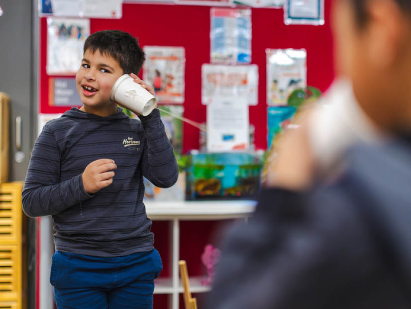Two boys smiling talking through a string and paper cup play telephone