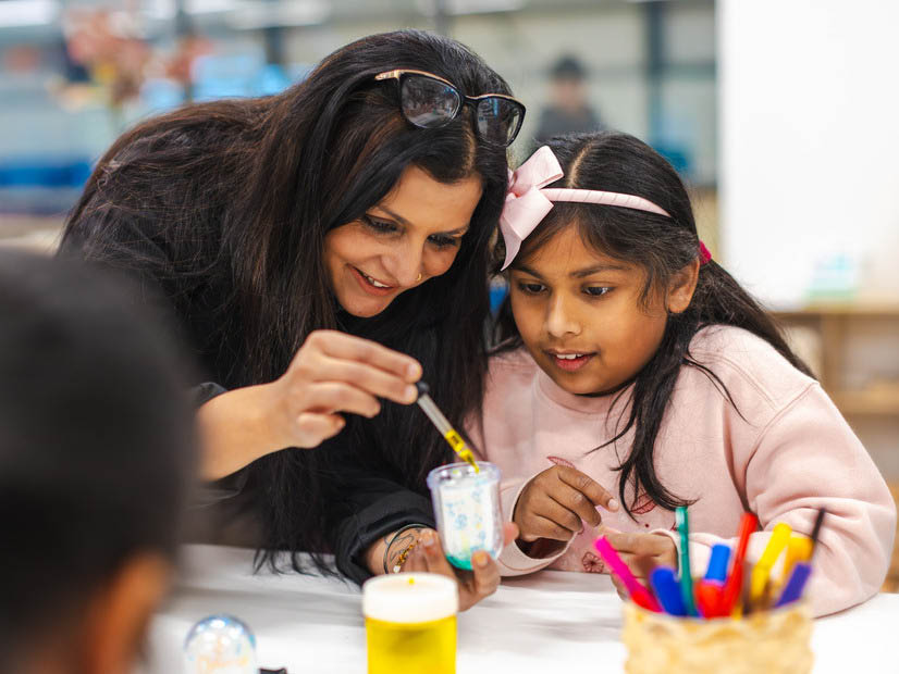 OSHC educator with girl a table doing a science experiment with a dropper of coloured liquid