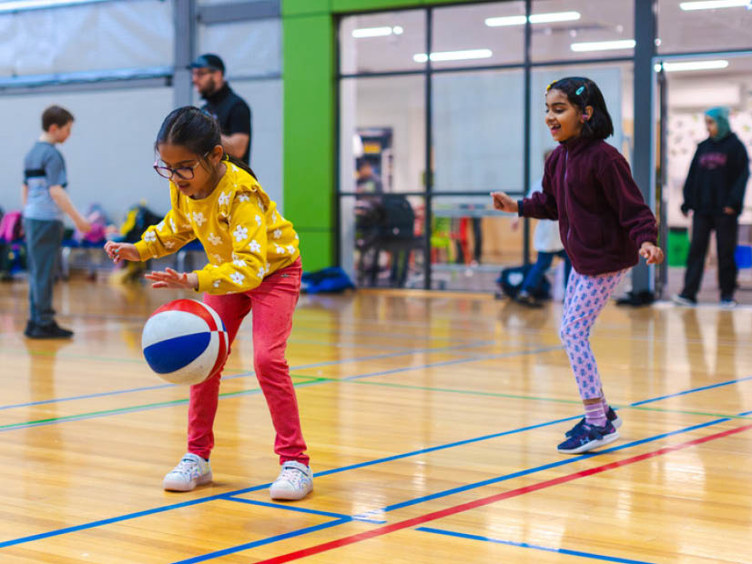 A girl bouncing a basketball in a stadium with OSHC educators an other kids in the background