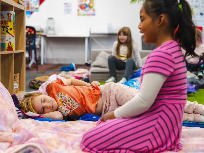 Two girls with blankets and pillows enjoying quiet time activity at OSHC