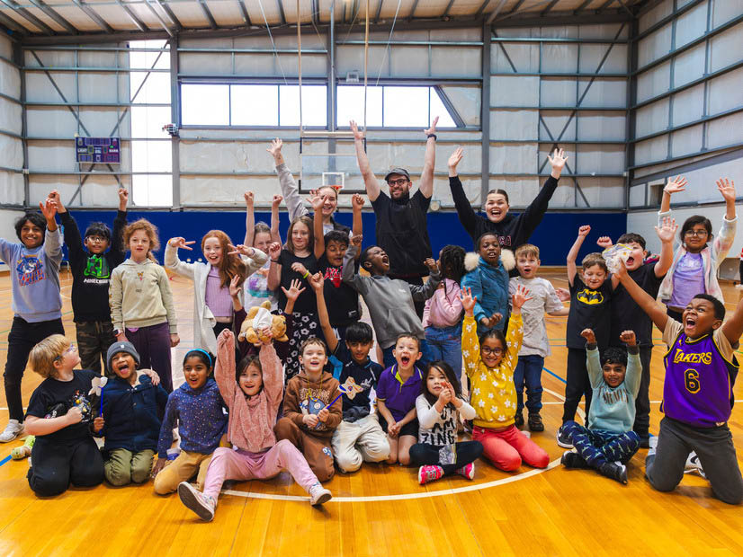 Happy group of kids and educators with hands in the air in stadium at holiday program