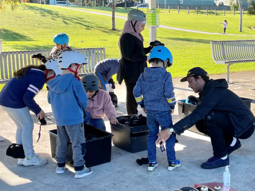 YMCA coach helps kids get gear on at holiday program skatebaording lesson